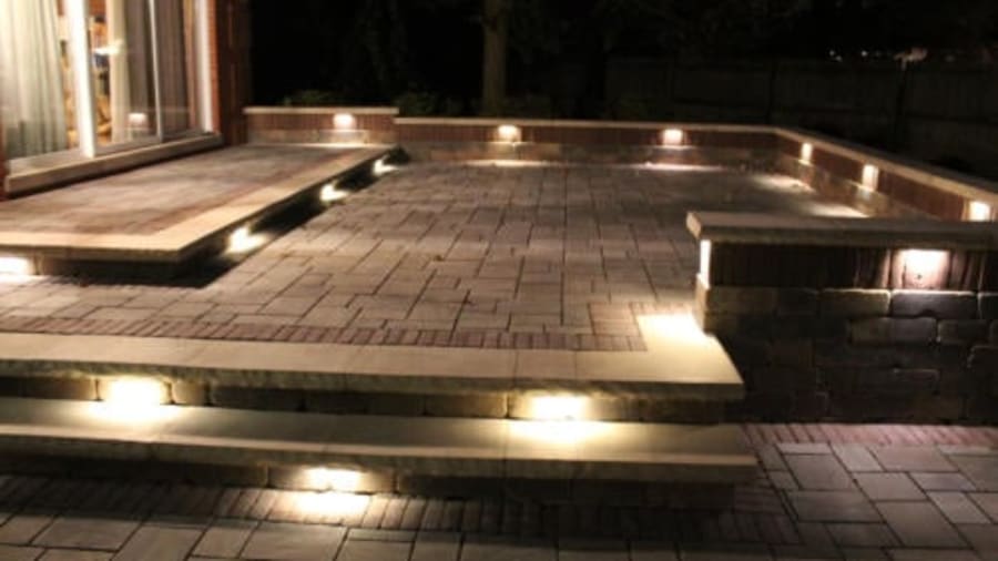 Backyard patio with stone pavers, steps, and built-in lights illuminating the area at night.